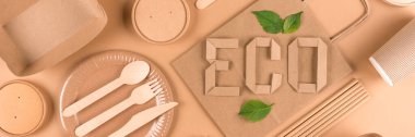 Paper utensils and wooden cutlery set with text ECO over light brown background. Street food sustainable paper packaging. Eco- friendly food containers, cups, plates and paper bag. Flat lay, banner