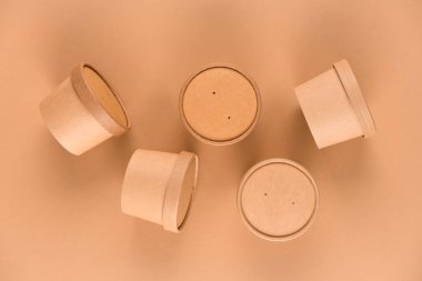 Many paper food containers, cups with paper cap over light brown background with copy space, mockup image. Sustainable food packaging. Monochrome, flat lay style
