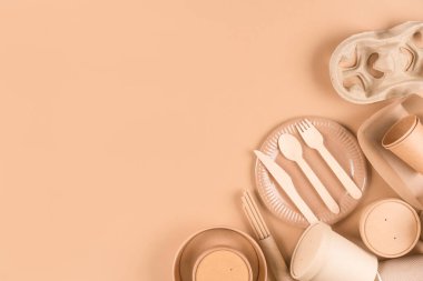 Paper utensils and tableware, wooden cutlery set, paper cups, plates, bags, pulp cup holders and food containers over light brown background with copy space. Sustainable food packaging concept