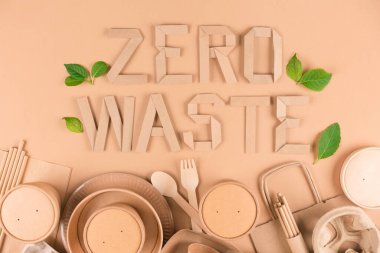 Eco food packaging concept, zero waste paper utensils over light brown background. Flat lay style. Text ZERO WASTE with green leaves around as a symbol of ecology production