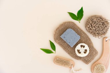 Bath accessories bundle for skin care and peeling. Skin exfoliation and scrubbing procedure - bath gloves, wooden brushes and organic soap scrub bar over light yellow background with copy space