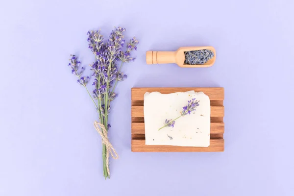 Natural herbal skin care products - organic handmade lavender soap or shampoo bar over purple background with lavender flowers. Natural herbal cosmetics with lavender extract, home body care. Flat lay