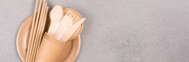 Banner, catering and eco utensils - paper plates and cups, wooden cutlery set and drinking straws over gray concrete background with copy space for your text. Sustainable food packaging