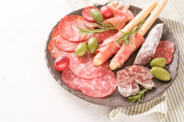 Charcuterie plate with variery of sausages - salami, bresaola, proscuitto served with olives and grissini over white table. Menu background with copy space. Traditional italian antipasti