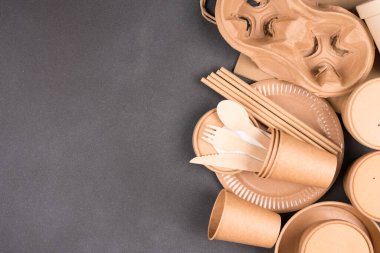 Paper utensils over dark concrete background with copy space - paper cups, food containers, bags and wooden bamboo cutlery set. Sustainable take away food packaging concept