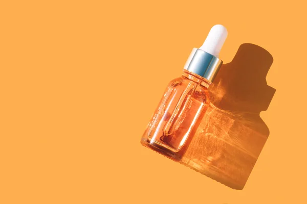 Natural face beauty oil with vitamin C. Glass dropper bottle with face serum over orange background with shadows and copy space, beauty skin-care products with natural ingredients and fruit essence. Mockup