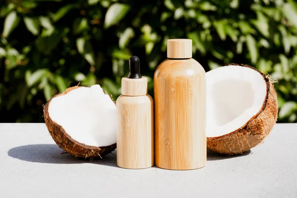 Coconut beauty products. Bottles with coconut cosmetic oil and body milk or lotion against natural green leaves background. Natural cosmetic treatment for skincare