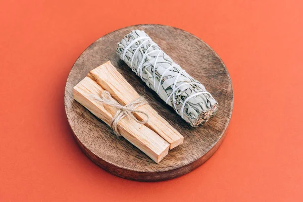 Incense bundle for meditation and room fumigation ritual. White sage and palo santo sticks on wooden podium over red background. Holy wood sticks. Selective focus