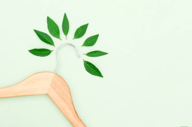 Wooden clothes hanger with green leaves over light green background with copy space as a symbol of slow fashion and environmentally friendly fashion. Reuse, recycling and upcycling clothes concept