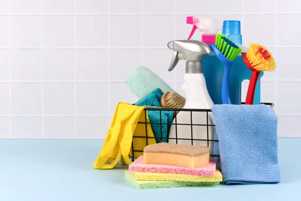 Different cleaning household supplies for bathroom against gray tiled wall with copy space. Cleaning service concept. Spray bottles with detergents and household chemicals