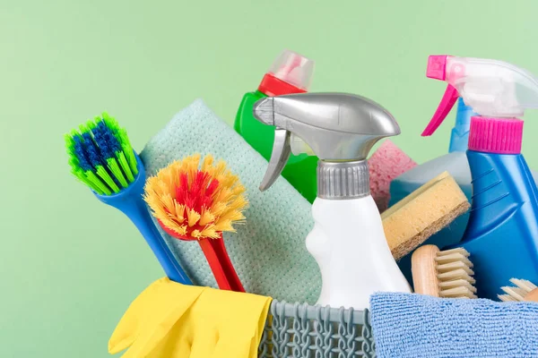 Closeup view of cleaning household supplies against green background. Cleaning service concept. Spray bottles with detergents and household chemicals