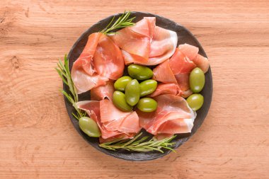 Ahşap masa arkasında zeytinli proscuitto ile servis edilen şarküteri tabağı. Geleneksel İtalyan antipastası. Seçici odak