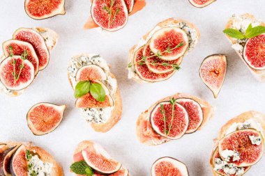 Birçok taze bruschetta ve kızarmış ekmek, çiğ incir, peynir, prosciutto ve otlar beyaz beton arka planda. Sağlıklı bir kahvaltı tarifi. Üst görünüm, seçici odaklanma. Düzleştirme biçimi