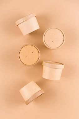 Çorba ya da dondurma için kahverengi kağıt yiyecek kapları, açık kahverengi arka planda kağıt kapaklı bardak, model resim. Sürdürülebilir gıda ambalajı. Tek Renkli