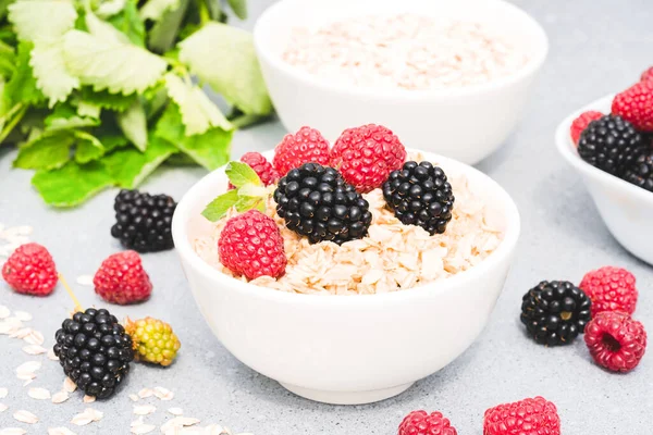 Oatmeal porridge served with berries and mint on concrete table background. Morning superfood porridge recipe. Healthy breakfast ideas