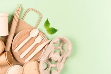 Eko kağıt çatal bıçaklar, ahşap çatal bıçak takımı, yiyecek kapları, kağıt bardaklar ve fotokopi alanı olan açık yeşil arka planda pipetler. Sürdürülebilir gıda paketleme kavramı