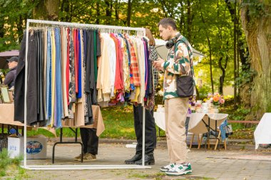 Lviv, Ukrayna - 29 Eylül. 2022: Genç hippi bit pazarından alışveriş yapıyor. Askıdaki kıyafetler - ikinci el kıyafet mağazası ya da ikinci el alışveriş konsepti. Seçici odak