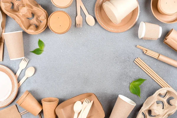 Paper utensils - paper cups, food containers, cup holders, paper straws, plates and wooden bamboo cutlery set over gray concrete background with copy space. Sustainable food packaging concept