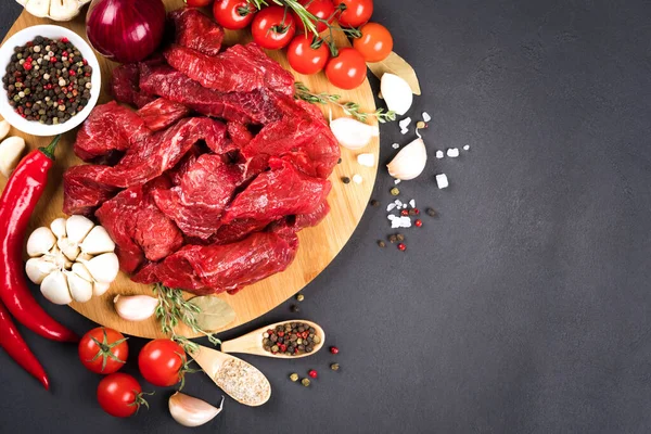 Chopped raw beef or lamb meat with spices, chili pepper and tomatoes over dark concrete background with copy space. Organic veal meat for cooking stew, azu or other meat main dish