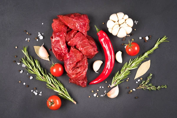 Chopped raw beef or lamb meat with seasonings, chili pepper and vegetables over dark concrete background. Organic veal meat for cooking stew, azu or other meat main dish