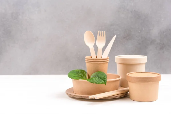 Sustainable food paper packaging.  Paper utensils - food paper containers, plates, wooden cutlery set against gray wall background with copy space. Eco tableware