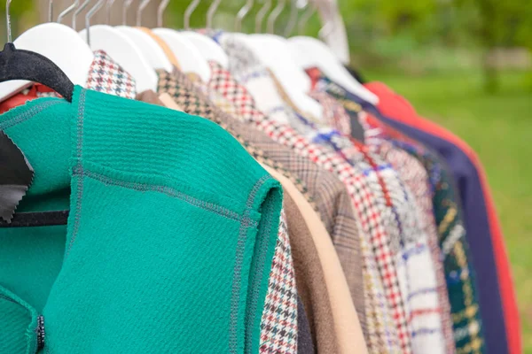 Clothes on hangers - second hand clothes store or thrift shopping concept. Clothing rental service. Selective focus. Car boot sale outside