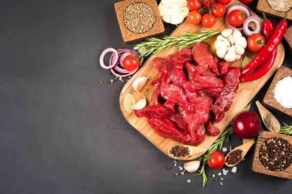 Chopped raw beef or lamb meat with spices, chili pepper and tomatoes over dark concrete background with copy space. Organic veal meat for cooking stew, azu or other meat main dish