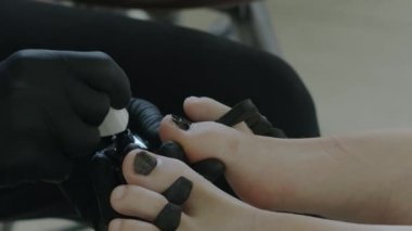 Siyah lateks ustası kızı pedikür yapıyor. Bacaklar yakın. Güzellik salonu ve ayak bakımı.