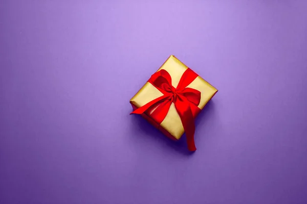 Dárek na dovolenou. Krabička ve zlatém dárkovém balení s červenou mašlí, na pantonovém pozadí. Veselé Vánoce, Valentýne. Pohlednice s láskou. — Stock fotografie