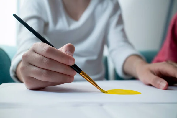 Barnens hand ritar gul sol på vitt papper. Ritar lektioner i skolan. Hemundervisning. Konst. Närbild av en borste. — Stockfoto