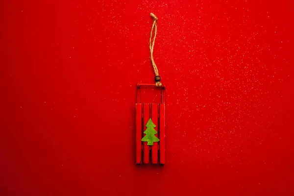 A toy sled on a festive tree, in honor of the New Year and Christmas. Red background. Greeting card. Imagem De Stock