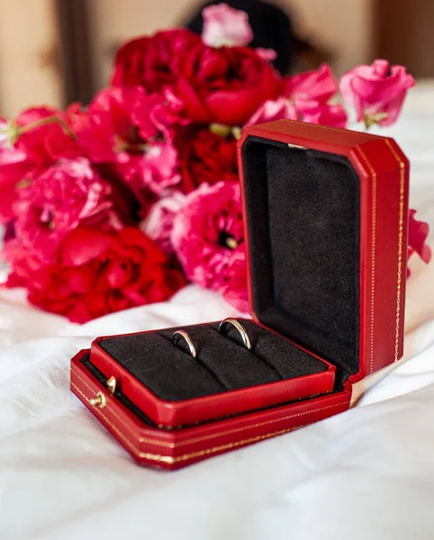 Due fedi nuziali d'oro sullo sfondo di un bouquet da sposa, in una scatola rossa. Vacanze. Fiori rosa. Immagine Stock