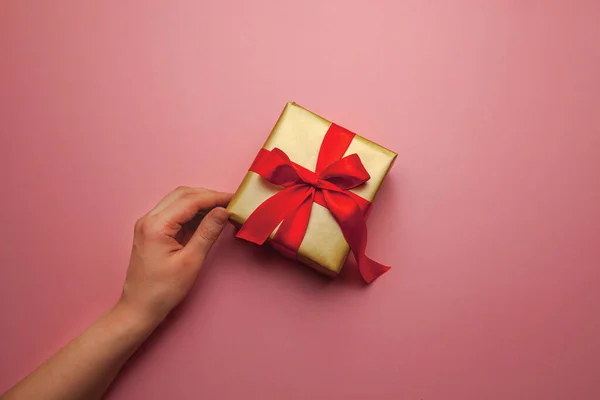 Regalo natalizio. Scatola in confezione regalo in oro con fiocco rosso, su fondo rosa. Buon Natale auguri di San Valentino. Cartolina con amore. Foto Stock