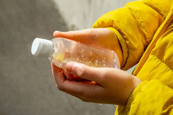 Egy gyerek sárga kabátban. A kezében egy üveg gél feldolgozására kezek baktériumok és vírusok. Alkoholtartalmú fertőtlenítő szer. — Stock Fotó