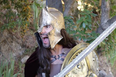 Doğada kılıç ve kalkan taşıyan şövalye kostümlü yakışıklı genç adamın yakın plan portresi.