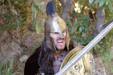 Doğada kılıç ve kalkan taşıyan şövalye kostümlü yakışıklı genç adamın yakın plan portresi.