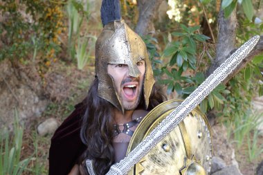 Doğada kılıç ve kalkan taşıyan şövalye kostümlü yakışıklı genç adamın yakın plan portresi.