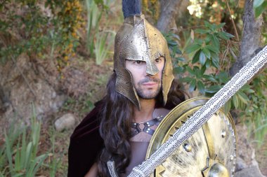 Doğada kılıç ve kalkan taşıyan şövalye kostümlü yakışıklı genç adamın yakın plan portresi.