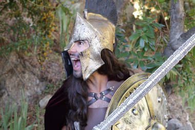 Doğada kılıç ve kalkan taşıyan şövalye kostümlü yakışıklı genç adamın yakın plan portresi.