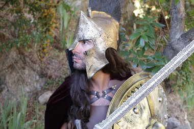 Doğada kılıç ve kalkan taşıyan şövalye kostümlü yakışıklı genç adamın yakın plan portresi.