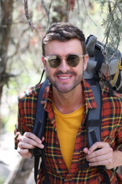 Doğada sırt çantalı, ekose gömlekli yakışıklı genç adamın portresi.