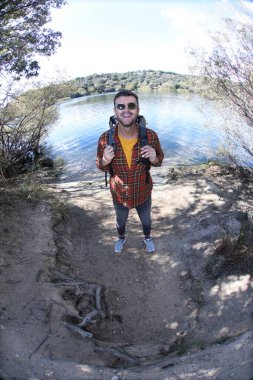 Doğada sırt çantalı, ekose gömlekli yakışıklı genç adamın portresi.