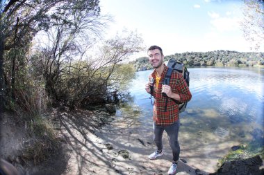 Doğada sırt çantalı, ekose gömlekli yakışıklı genç adamın portresi.