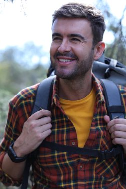 Doğada sırt çantalı, ekose gömlekli yakışıklı genç adamın portresi.