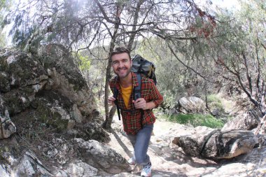 Doğada sırt çantalı, ekose gömlekli yakışıklı genç adamın portresi.