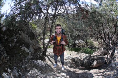 Doğada sırt çantalı, ekose gömlekli yakışıklı genç adamın portresi.