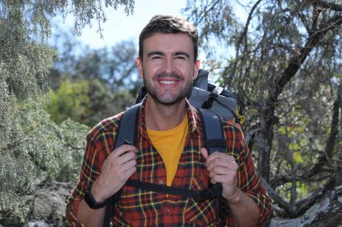 Doğada sırt çantalı, ekose gömlekli yakışıklı genç adamın portresi.