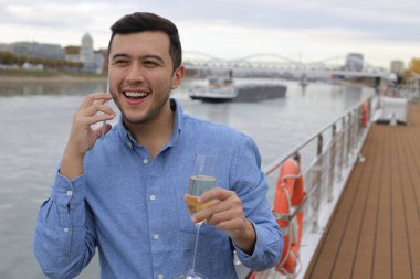 Bir bardak şampanyayla güvertede telefonla konuşan yakışıklı genç adamın portresi.