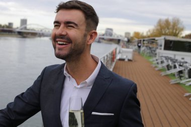 Bir bardak şampanyası olan yakışıklı bir gencin portresi geminin güvertesinde duruyor.