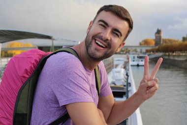 Sırt çantasıyla seyahat ederken barış jesti yapan yakışıklı bir gencin portresi